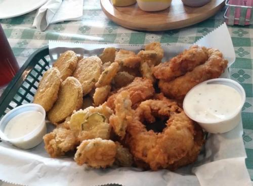 A basket of fried food including onion rings, fried pickles, and golden fried slices, served with dipping sauces.