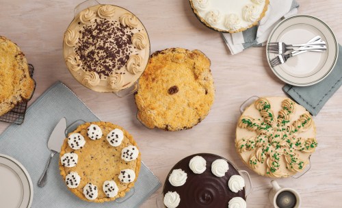 An assortment of cakes and pies on a table, featuring various toppings and decorations, with plates and utensils nearby.