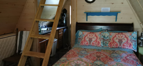 Cozy cabin interior featuring a colorful bedspread, wooden ladder, and kitchenette in a rustic setting.