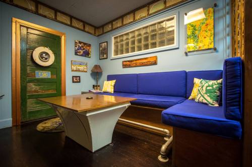 Cozy room with blue seating, a wooden table, and colorful artwork on the walls, featuring a green door.
