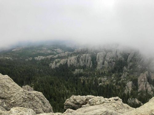 A misty view of rugged mountains and dense forests, with clouds partially obscuring the landscape.