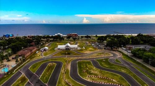Aerial view of a go-kart track near the ocean, with lush greenery and a clear blue sky in the background.