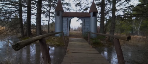 A wooden bridge leads to a whimsical castle entrance surrounded by trees and a misty landscape.