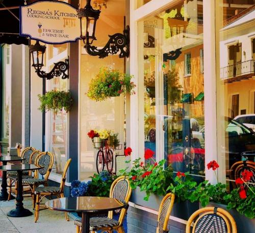 A charming cooking school with outdoor seating, flower baskets, and vibrant red geraniums in a quaint street setting.