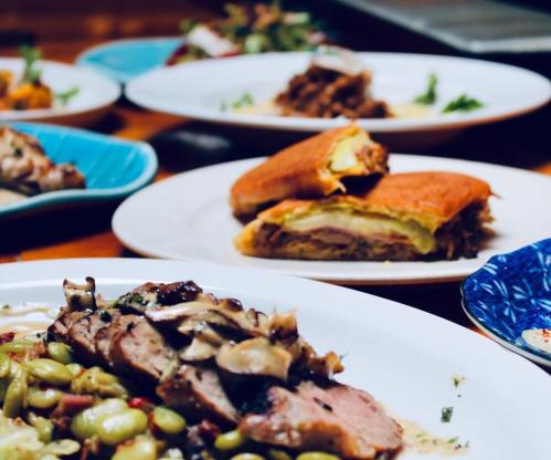 A close-up of a plate featuring sliced meat with mushrooms, alongside a sandwich and various dishes in the background.