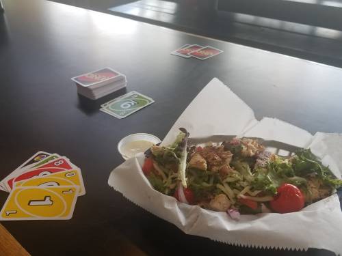 A plate of grilled chicken salad with tomatoes and a dipping sauce, alongside a deck of Uno cards on a table.