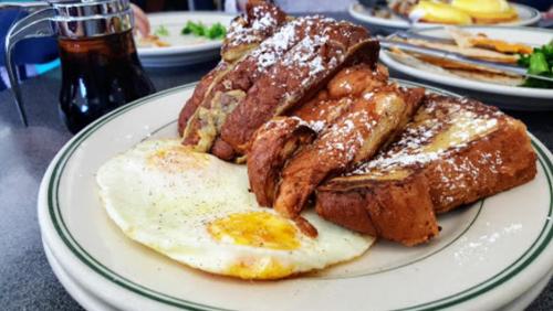 A plate featuring French toast dusted with powdered sugar, served with a sunny-side-up egg and syrup on the side.