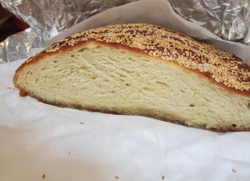 A loaf of bread with a golden crust and sesame seeds on top, resting on white parchment paper.