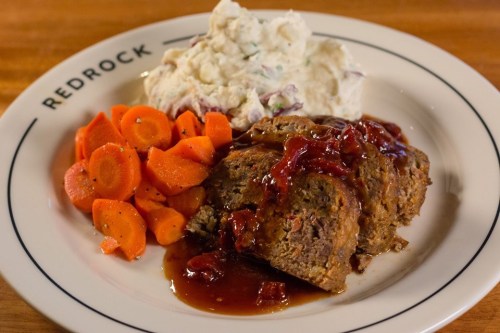 A plate featuring meatloaf with sauce, mashed potatoes, and seasoned carrots.
