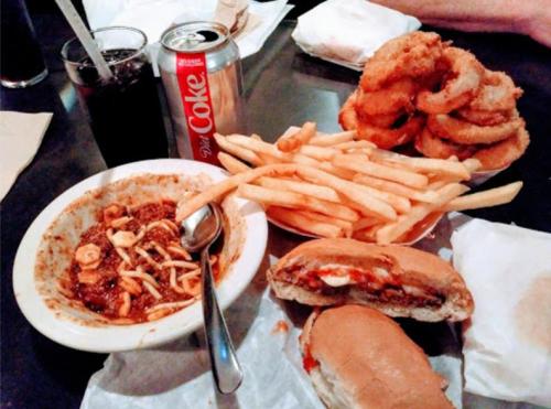 A table with a bowl of chili, two sandwiches, fries, onion rings, and a can of Diet Coke.