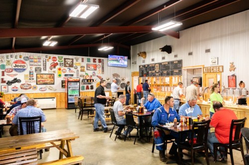 A busy restaurant interior with patrons dining, a menu board, and vintage signs on the walls.