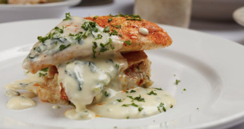 A plate of fish topped with creamy sauce and herbs, served over a bed of rice or bread.