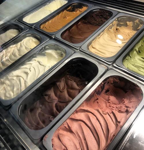 A display of various gelato flavors in metal containers, including chocolate, vanilla, and green tea.