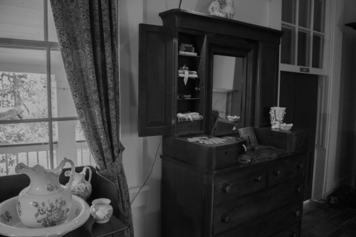 A vintage wooden dresser with a mirror, displaying small items, beside decorative porcelain pieces and a patterned curtain.