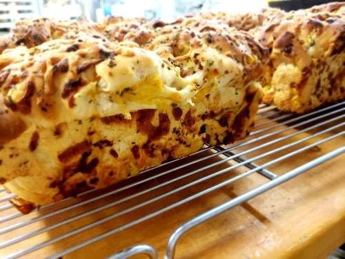 Freshly baked bread cooling on a wire rack, with a golden crust and herbs visible on the surface.
