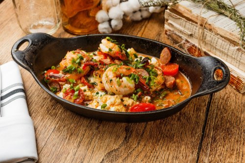 A cast-iron skillet filled with shrimp, sausage, and vegetables, garnished with green onions on a wooden table.