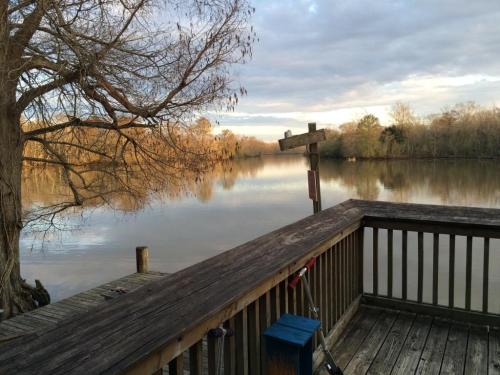 A serene river scene at sunset, with a wooden deck, trees, and calm water reflecting the sky.