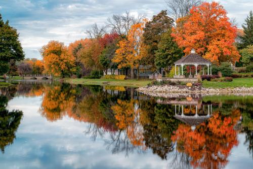 A serene lake reflects vibrant autumn trees and a gazebo, creating a picturesque fall landscape.