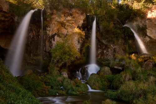 A serene waterfall cascades over rocky cliffs, surrounded by lush greenery and tranquil pools.