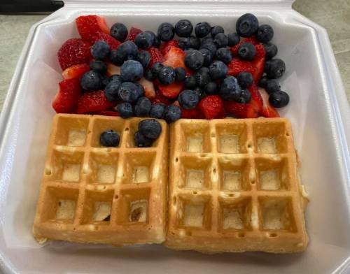 A takeout container with two waffles and a mix of fresh strawberries and blueberries on the side.
