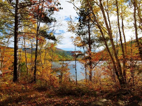 A serene lake surrounded by vibrant autumn foliage and trees under a partly cloudy sky.
