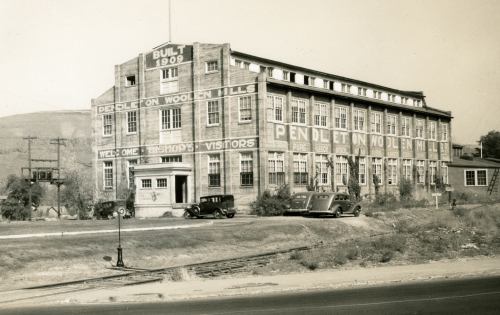 Historic Pendleton Woolen Mills building from 1909, featuring vintage cars parked outside and a scenic backdrop.