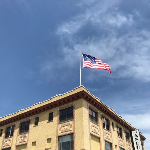 A U.S. flag waves atop a historic building against a blue sky with scattered clouds.