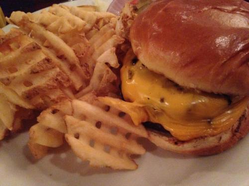 A juicy cheeseburger with melted cheese, served with a side of crispy waffle fries on a white plate.