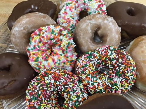 A variety of colorful donuts on a glass platter, including chocolate, glazed, and sprinkles.