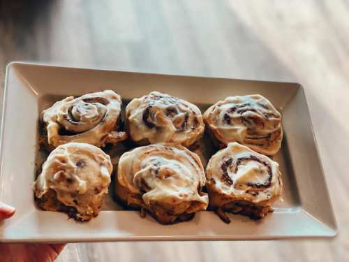 A plate of six freshly baked cinnamon rolls topped with creamy icing.