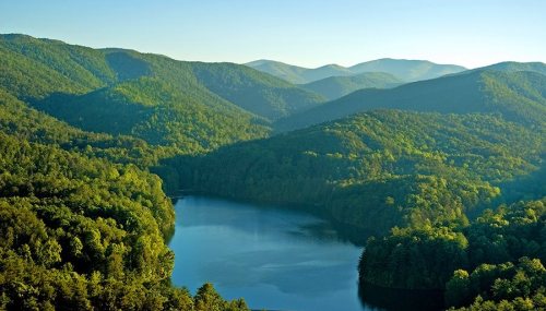 A serene landscape featuring lush green mountains surrounding a calm lake under a clear blue sky.