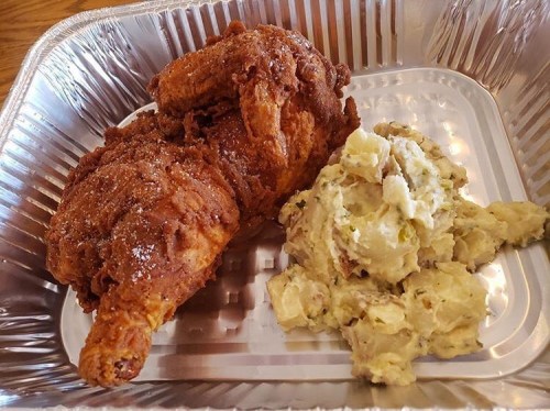 A serving of crispy fried chicken with a side of creamy mashed potatoes in a silver takeout container.