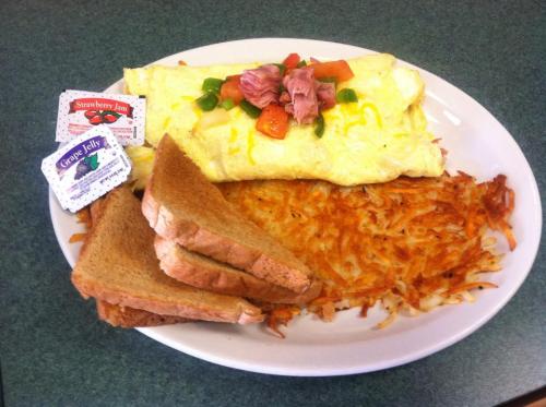 A plate of fluffy omelette topped with ham and vegetables, served with toast and hash browns, alongside jam packets.