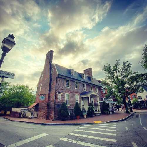 Historic brick building at a street corner, with trees and a cloudy sky in the background.