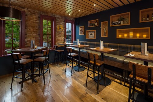 Cozy restaurant interior with wooden tables, chairs, and a brick wall, featuring warm lighting and decorative frames.
