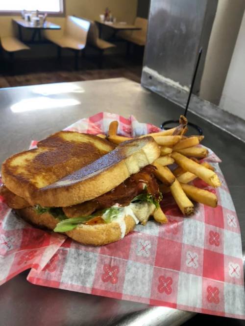 A grilled sandwich with lettuce and sauce, served with a side of golden French fries on a red checkered paper.