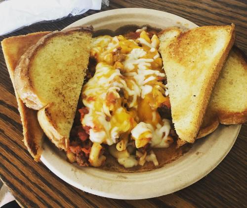 A bowl of cheesy pasta topped with meat, surrounded by slices of toasted bread.