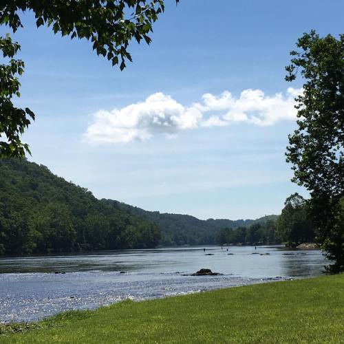 A serene river flows through lush green hills under a clear blue sky with a few clouds.