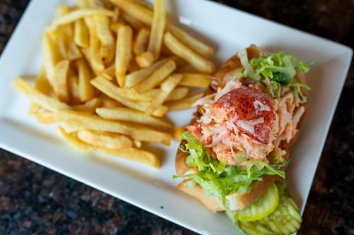 A lobster roll topped with lettuce and served with a side of golden French fries on a white plate.