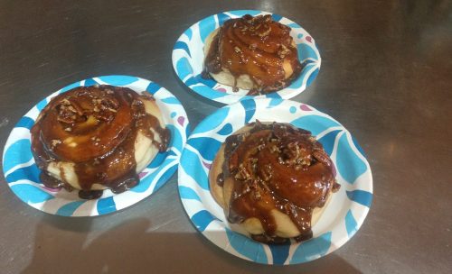 Three cinnamon rolls topped with caramel and pecans, served on colorful paper plates.