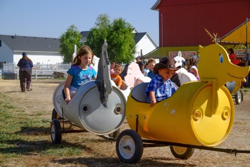 Children ride in colorful animal-shaped carts at a farm, enjoying a sunny day of fun and play.