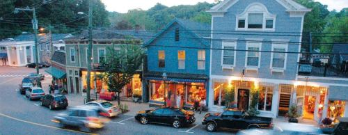A charming street scene at dusk, featuring quaint shops and parked cars along a tree-lined road.
