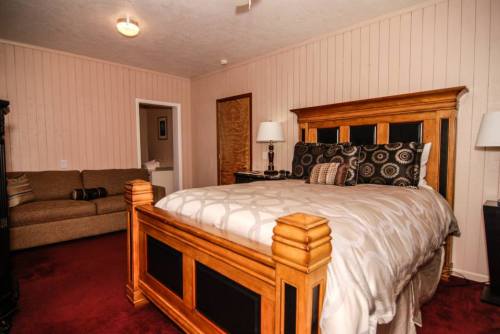 Cozy bedroom featuring a wooden bed, patterned bedding, a sofa, and warm wall colors.