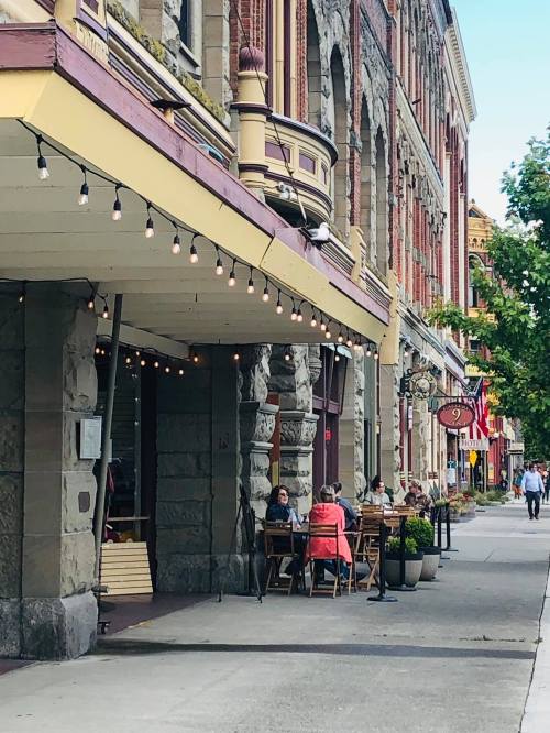 Outdoor café scene with patrons at tables, string lights overhead, and historic buildings lining the street.