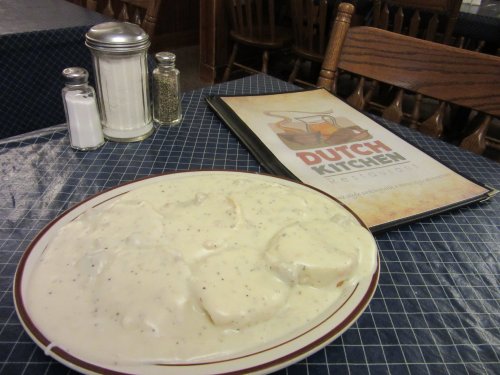 A plate of biscuits smothered in creamy gravy, with a menu and condiments on a checkered tablecloth.