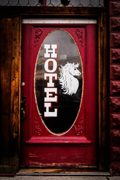 A red door with an oval window featuring the word "HOTEL" and a white unicorn illustration.