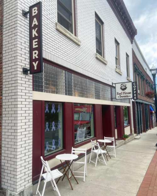A bakery storefront with a sign, outdoor seating, and a neighboring shop in a quaint street setting.
