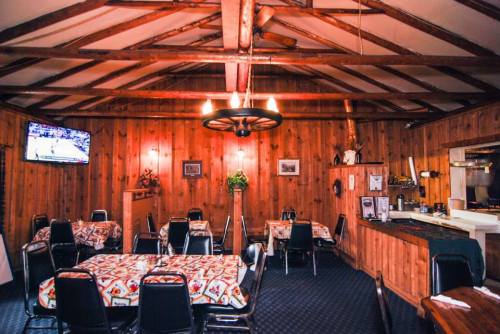 Cozy restaurant interior with wooden walls, tables covered in patterned cloths, and a TV mounted on the wall.