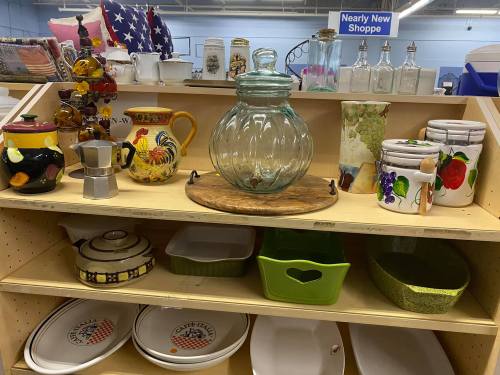 A wooden shelf displays various colorful kitchenware, including glass jars, ceramic pots, and decorative dishes.