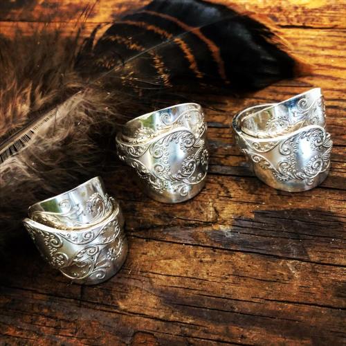 Three intricately designed silver rings on a rustic wooden surface, accompanied by a feather.